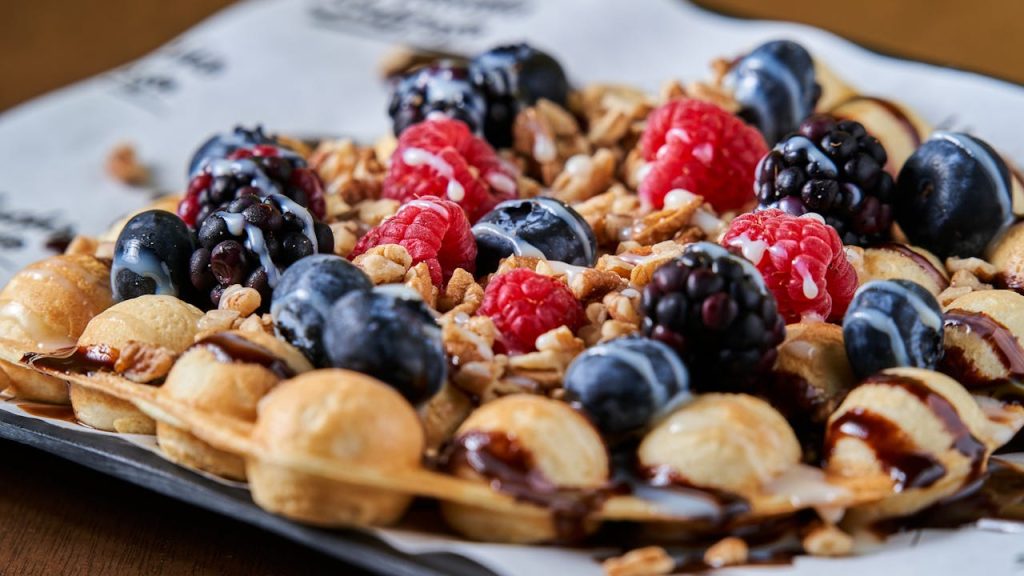 Delicious bubble waffles topped with fresh raspberries, blueberries, and nuts.